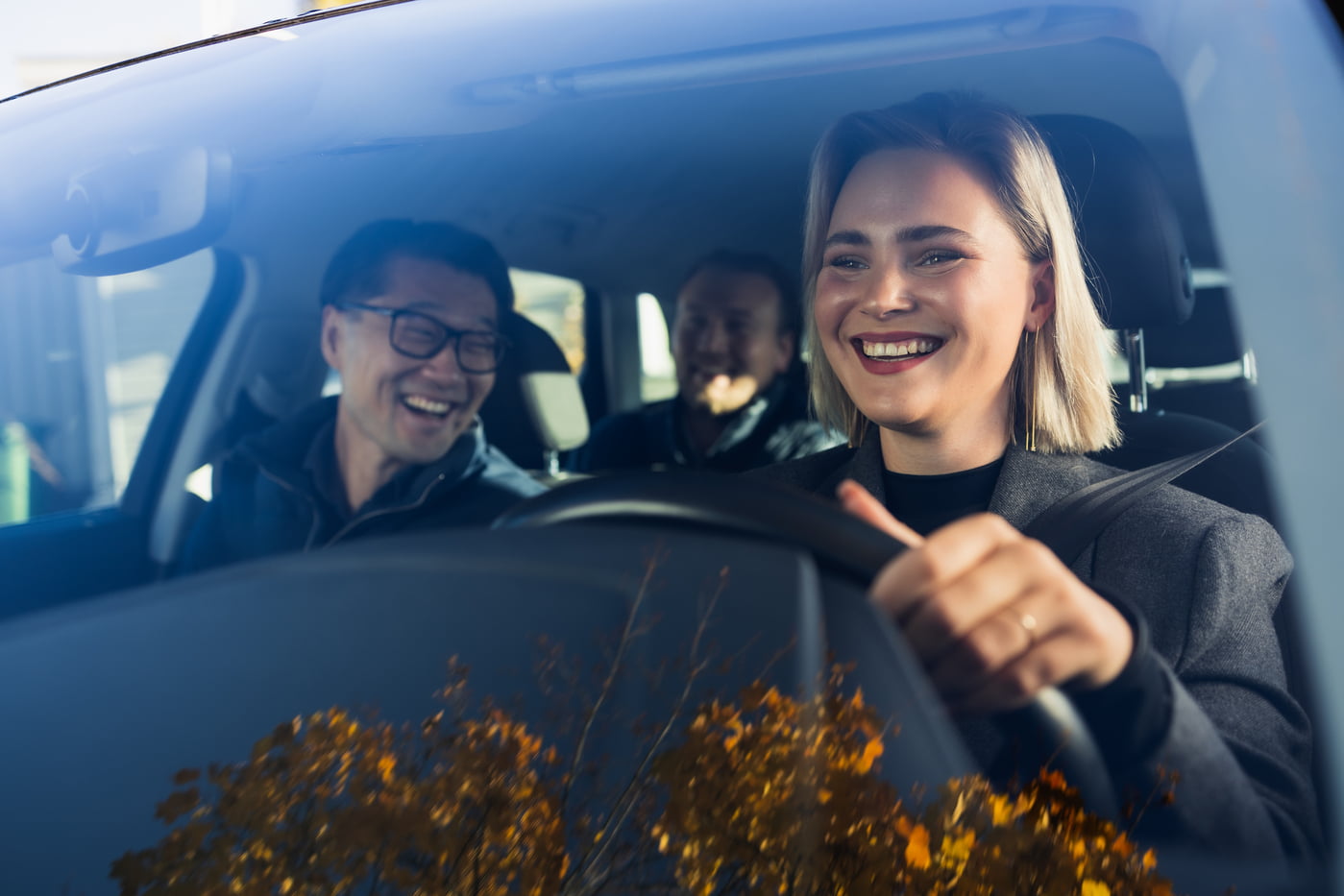 Blid dame som kjører bil med to mannlige passasjerer