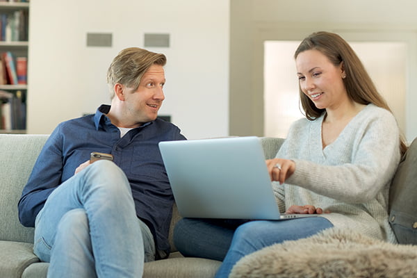 Smilande mann og kvinne som sit i ein sofa og ser på ei bærbar datamaskin